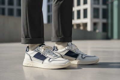 White sneakers with blue accents worn by a person on a concrete surface with a blurred building background